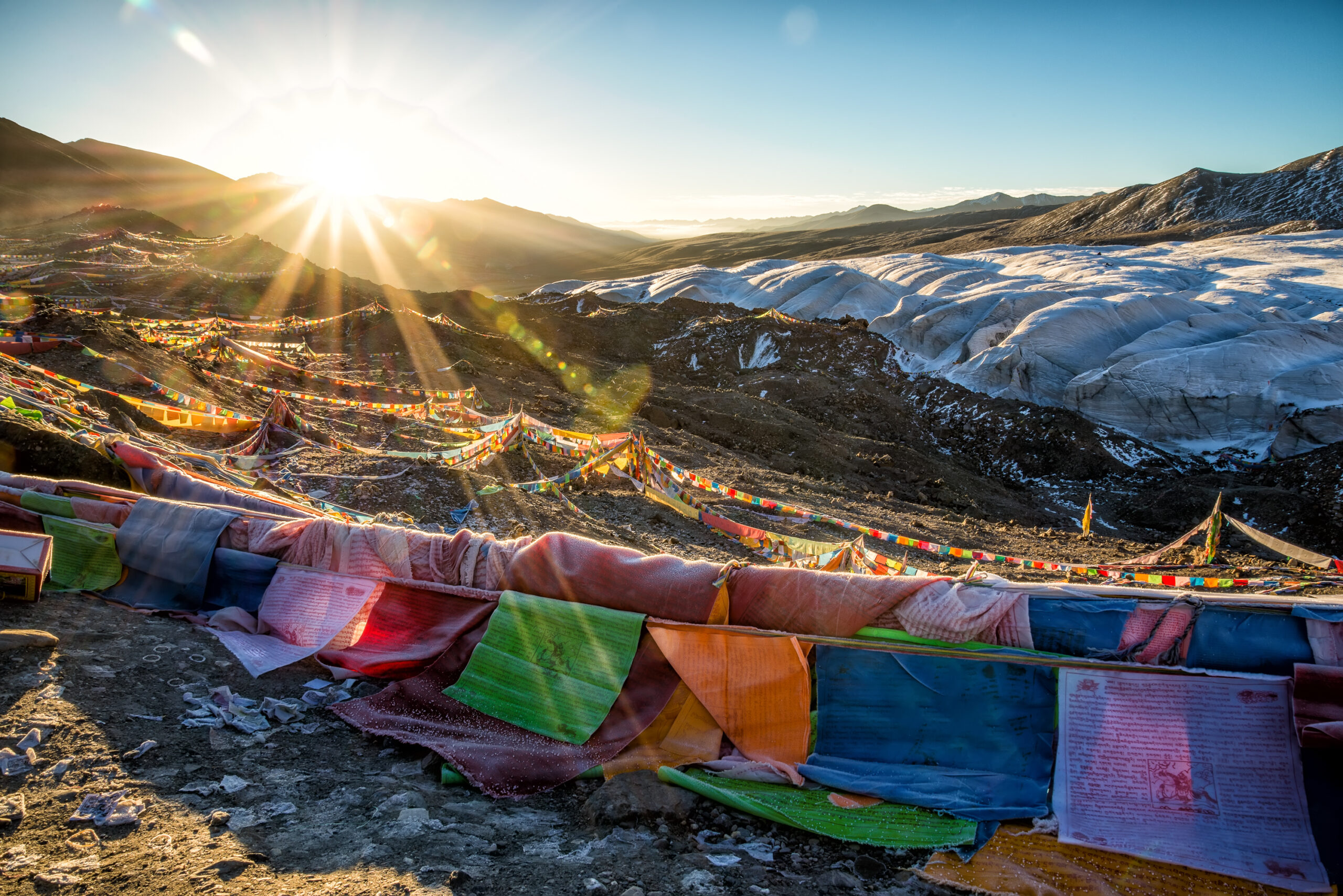 Golden sunrise illuminating snow-clad Himalayan peaks with vibrant Buddhist prayer flags fluttering in the mountain air — a divine glimpse of Sikkim’s spiritual beaut